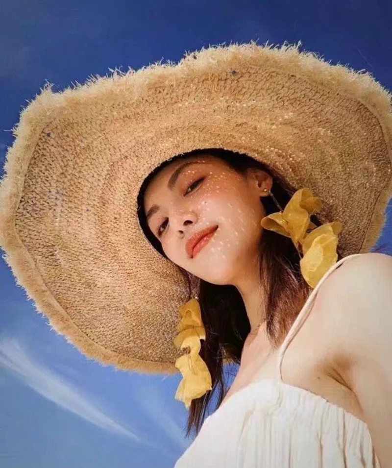 Web-kendte med stor lafite græs udhæng den stilfulde parasol hat den kvindelige sea beach resort er forhindret sole sig i stråhat